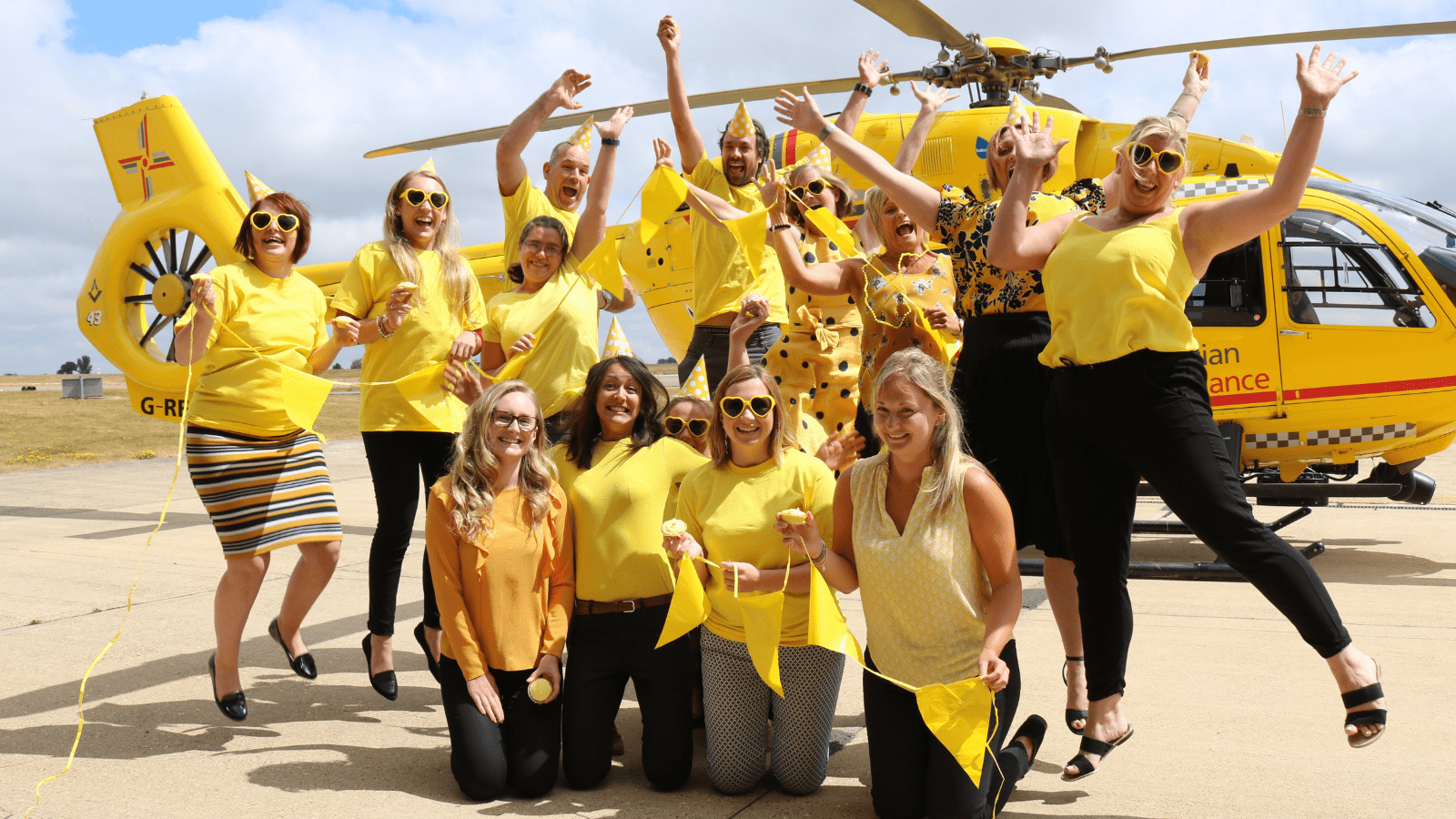 Group of people taking part in EAAA's 'Get Up and Go Yellow' and wearing yellow in front of yellow helicopter